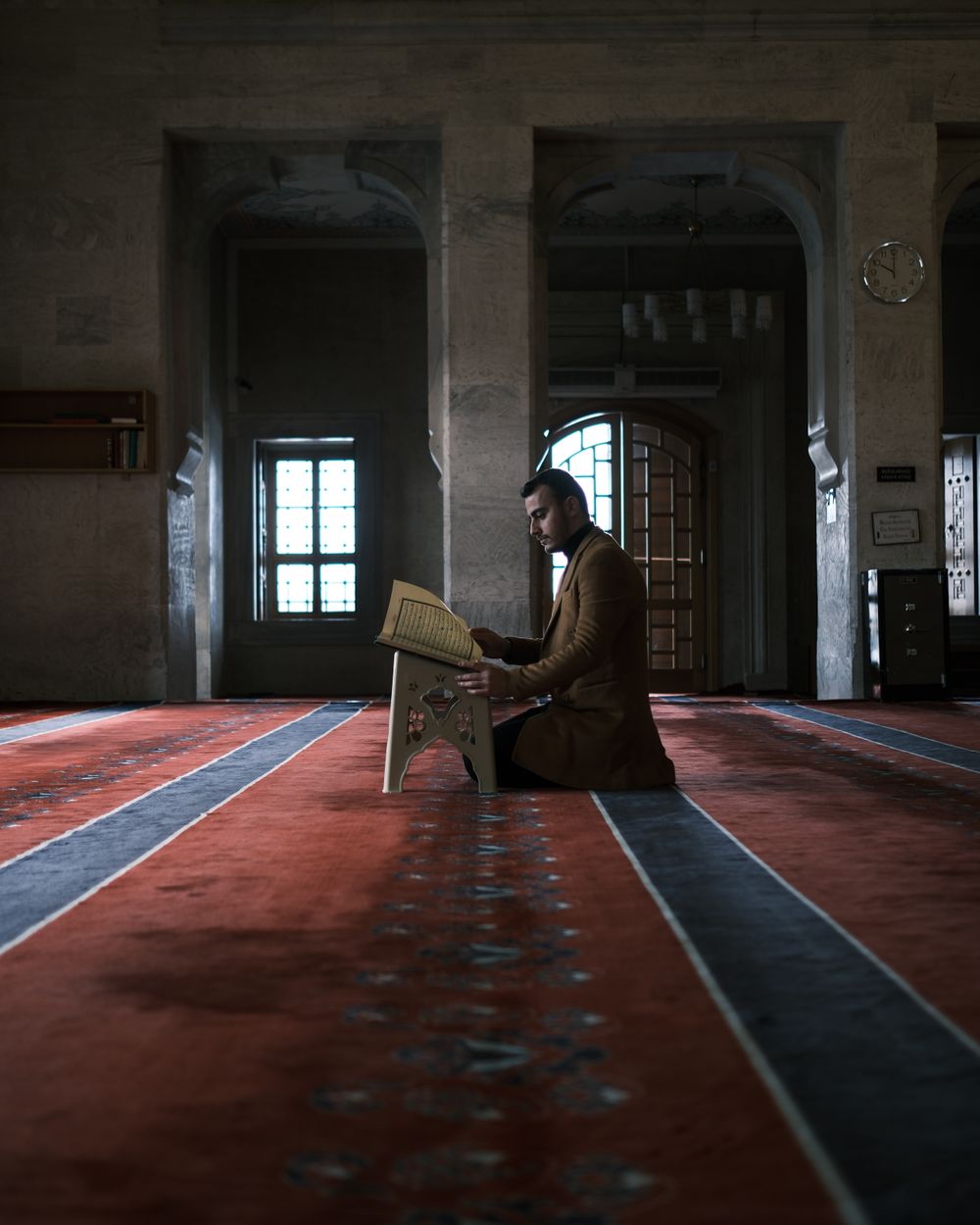 رجل يقرأ القرآن الكريم في مسجد بإضاءة دافئة